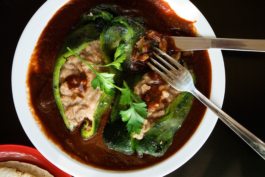 Bean stuffed poblano peppers in a mild red chile salsa served on a white plate.