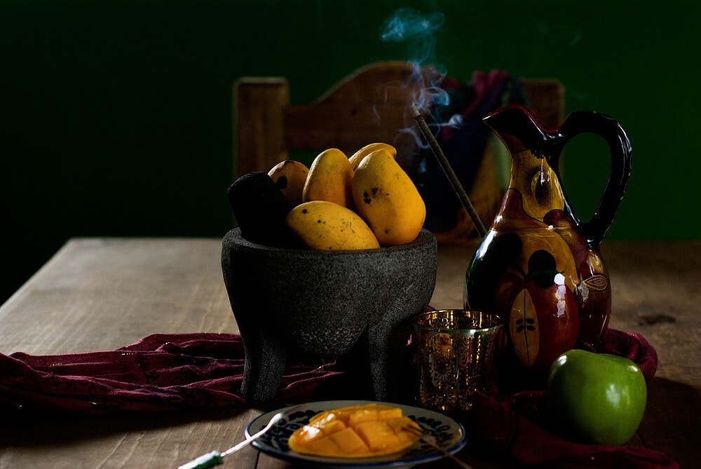 A big bowl full of mangoes on a dark brown table. 