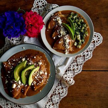 Two plates with vegan enfrijoladas, which are like enchiladas but with a creamy bean sauce.