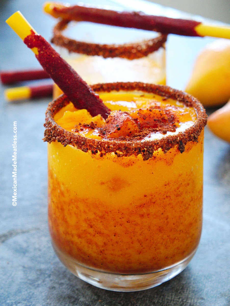 Small glass rimmed with chile powder and mangonada mango slushy inside with a tamarind candy stick. 