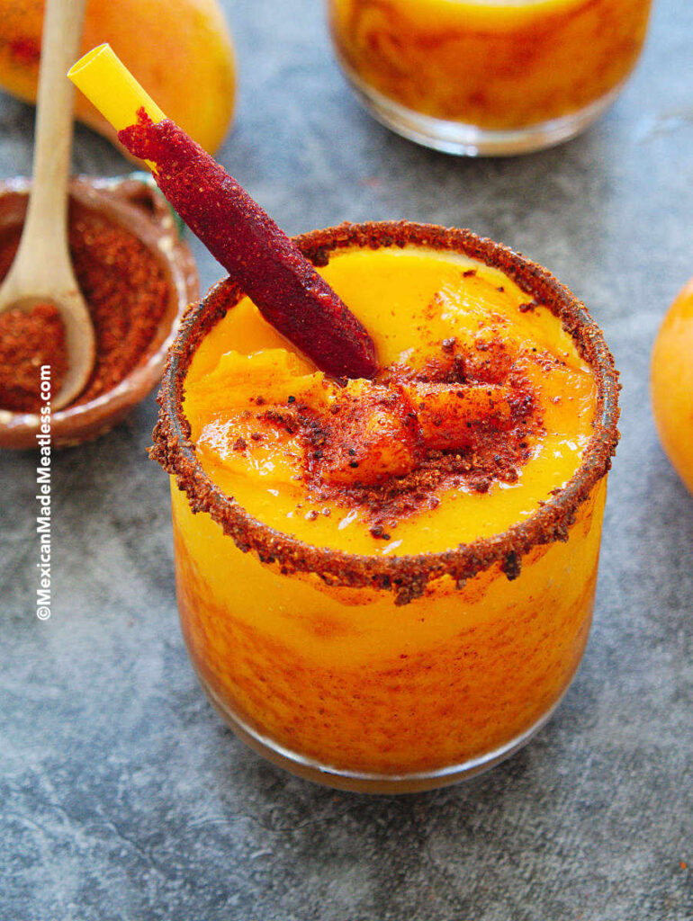 Mexican frozen mango sorbet drink called mangonada in a glass and drizzled with chamoy and Tajin. 