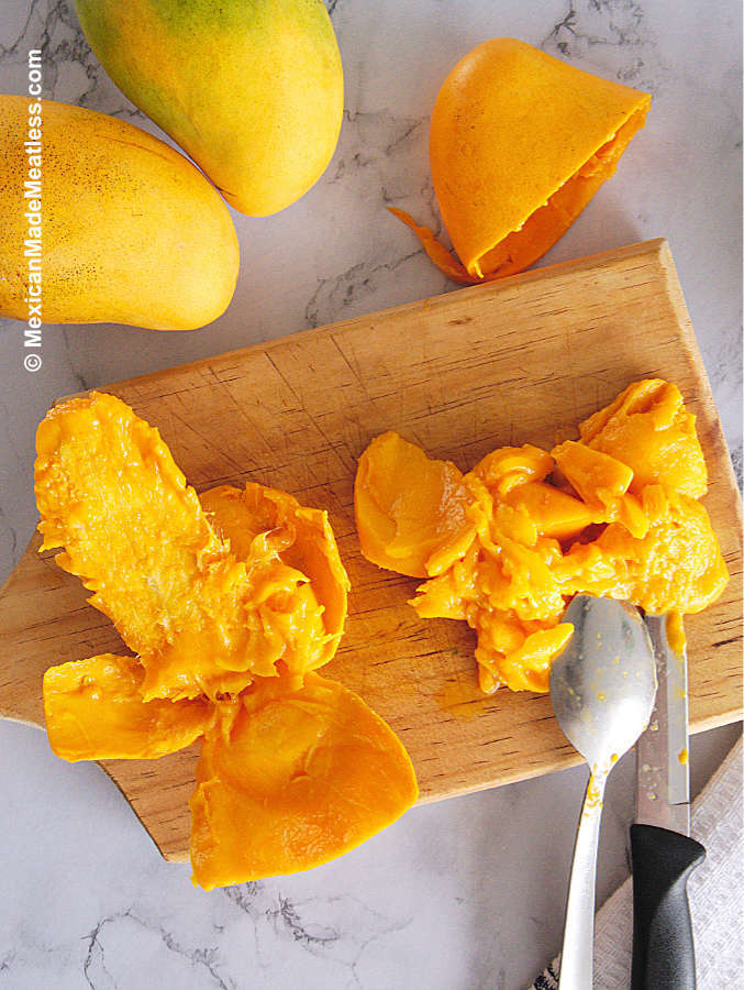 Showing a cutting board with a small yellow mango and showing how to eat it.