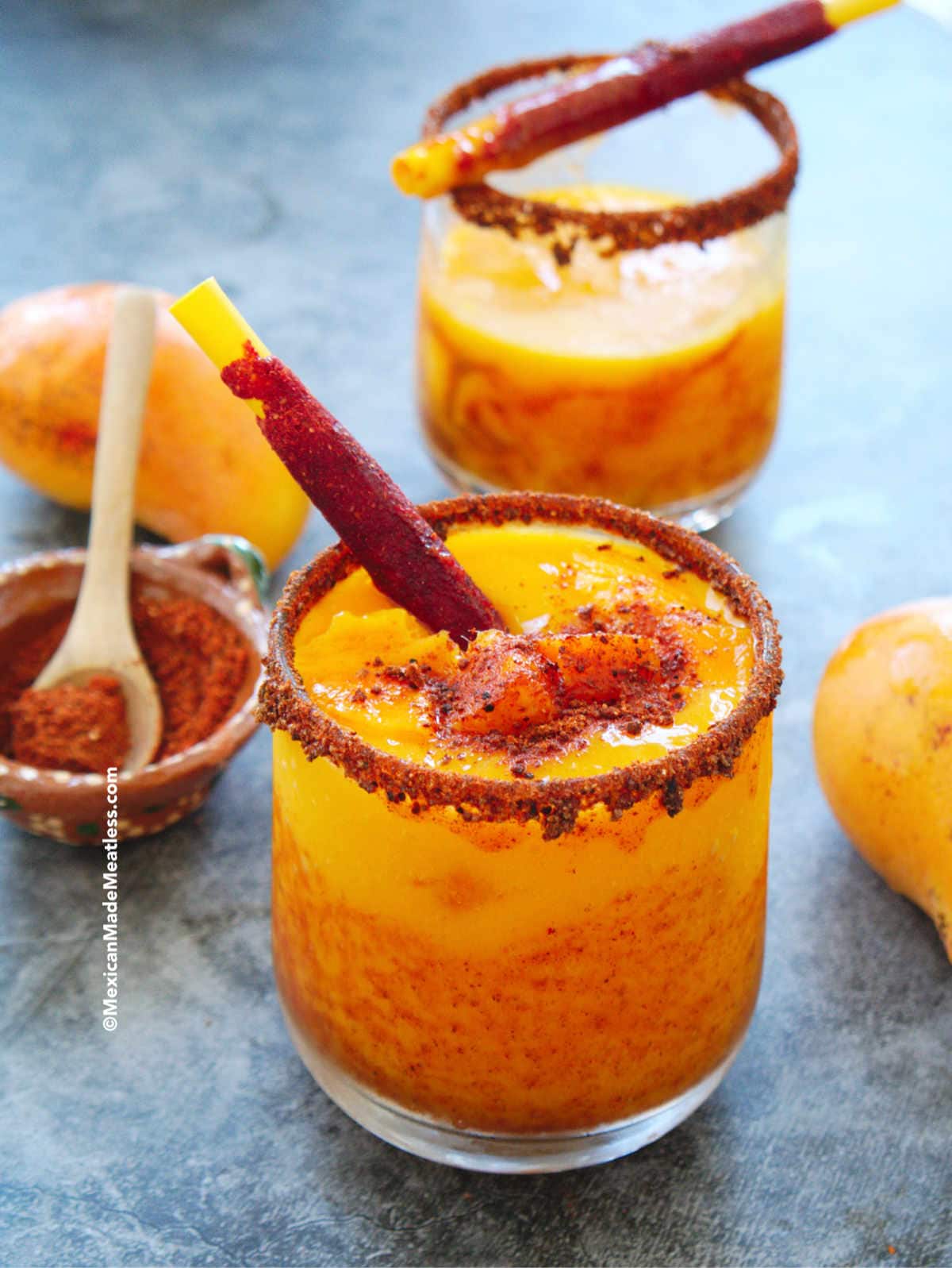 Two glasses full of Mexican frozen mango drinks with chamoy sauce, called mangonadas.