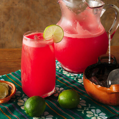 A pitcher and glass of ice cold watermelon agua fresca.