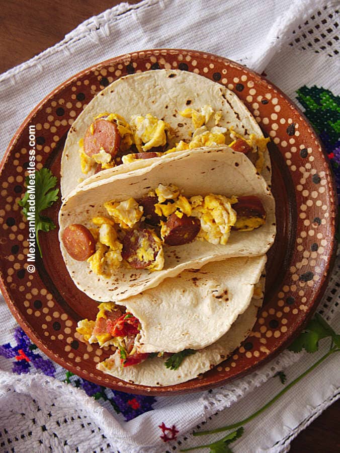 Brown plate with 3 breakfast tacos filled with eggs and vegan hot dogs.