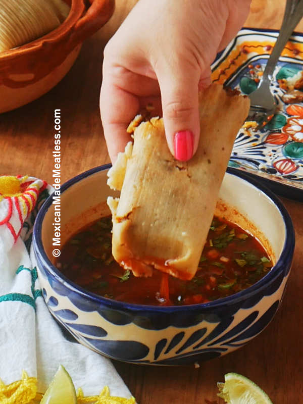 Homemade birria tamales being dipped into a bowl of birria consome broth.