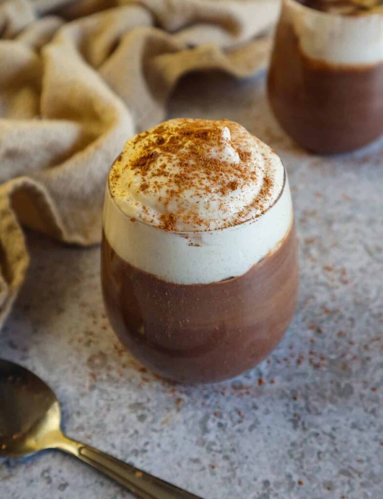 Vegan chocolate pudding with whipped cream served inside a small glass.