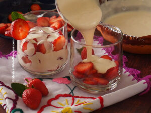 Layering sliced strawberries with sweet cream into a clear glass cup.