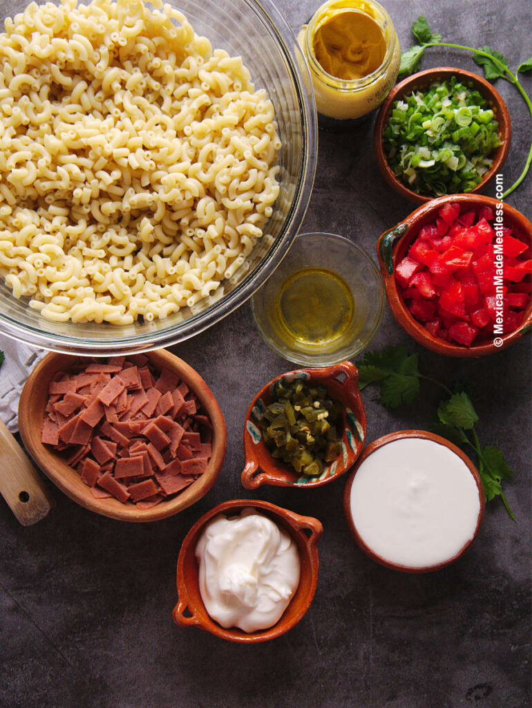 Ingredients for making Mexican macaroni salad. They are elbow macaroni, onion tomato, ham, sour cream, mayonnaise, jalapenos and spices.