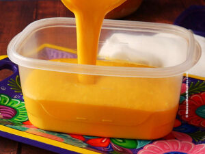 Pouring homemade mango ice cream into a freezer safe container.