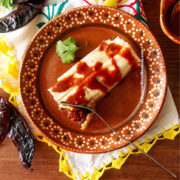 One tamale with red salsa drizzled over it on top of a decorative Mexican plate.