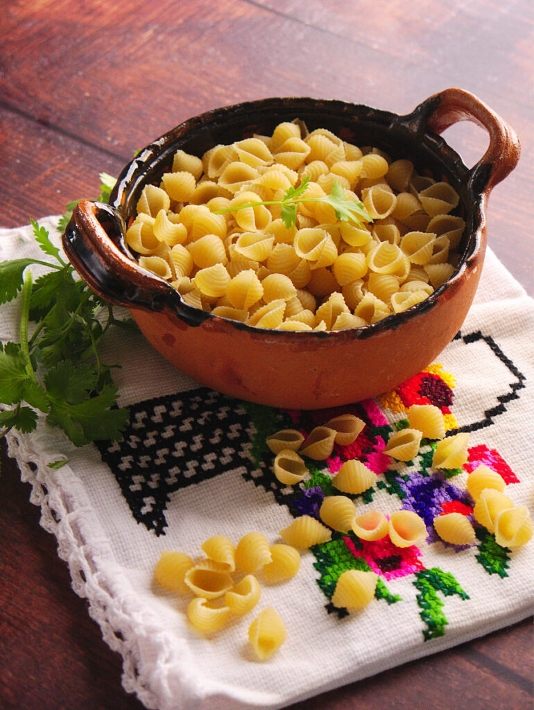 Shell pasta for sopa de conchas in a small brown bowl.