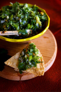 Spicy and chunky roasted habanero salsa made with garlic and cilantro served in a small bowl and corn chips.
