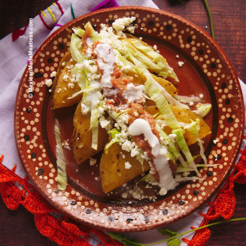 A plate on top of a white and orange kitchen towel, on the plate are 3 crispy fried potato tacos that are topped with lettuce, cheese, salsa and sour cream.