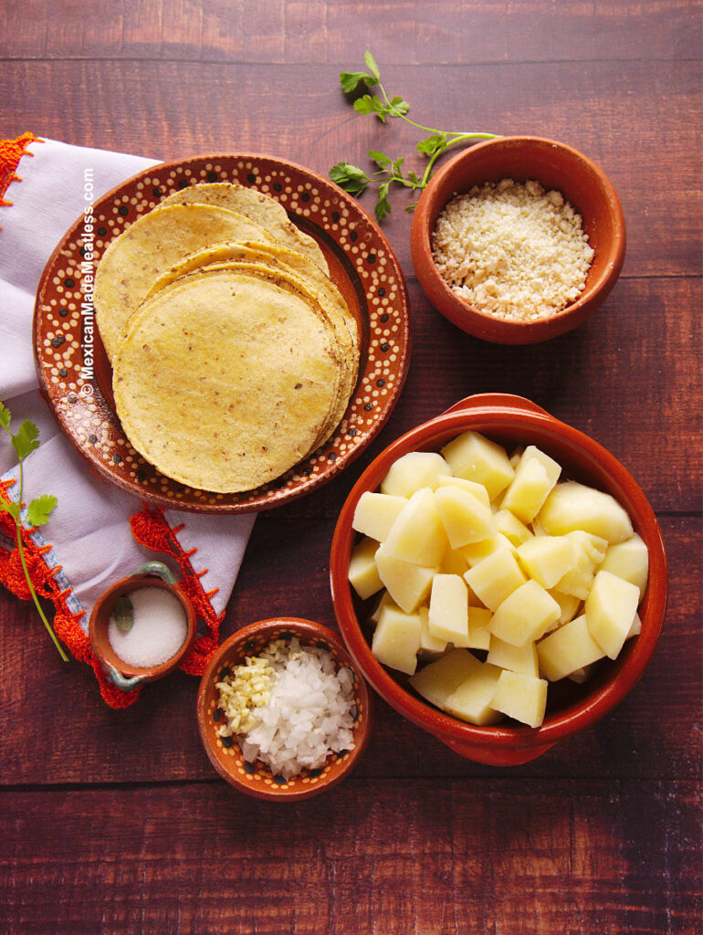 Ingredients to make Mexican tacos de papa. There are warm corn tortillas, boiled potatoes, onion, garlic, salt and crumbled cheese.