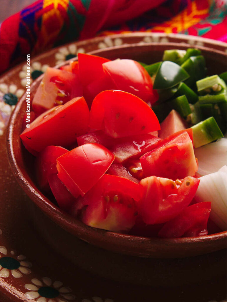 Fresh ripe red tomatoes in a small bowl with jalapenos and onion.