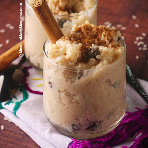 Clear glass filled with Mexican vegan arroz con leche or rice pudding. It has raisins and is sprinkled with cinnamon.
