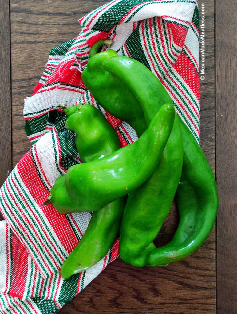 Four fresh green hatch chiles on a red and white kitchen cloth.
