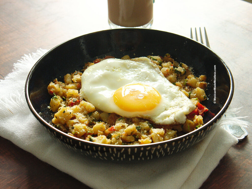 A dark blue bowl filled with Mexican potatoes and a sunny side up egg on top. 