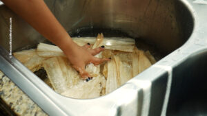 Hydrating corn husks in hot water in a sink.