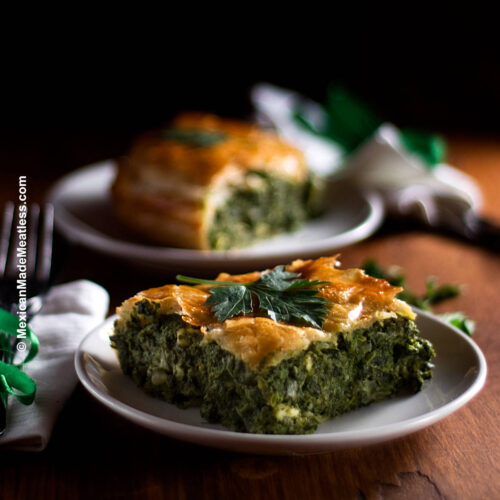 Two white plates with slices of Spanakopita or Greek spinach pie.
