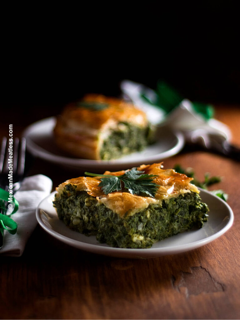 Two white plates with slices of Spanakopita or Greek spinach pie. 