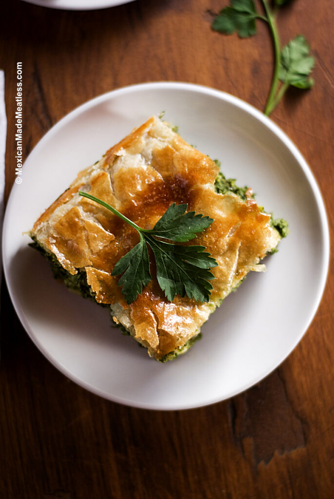 White plate with square piece of Greek spinach pie with flaky puff pastry. 
