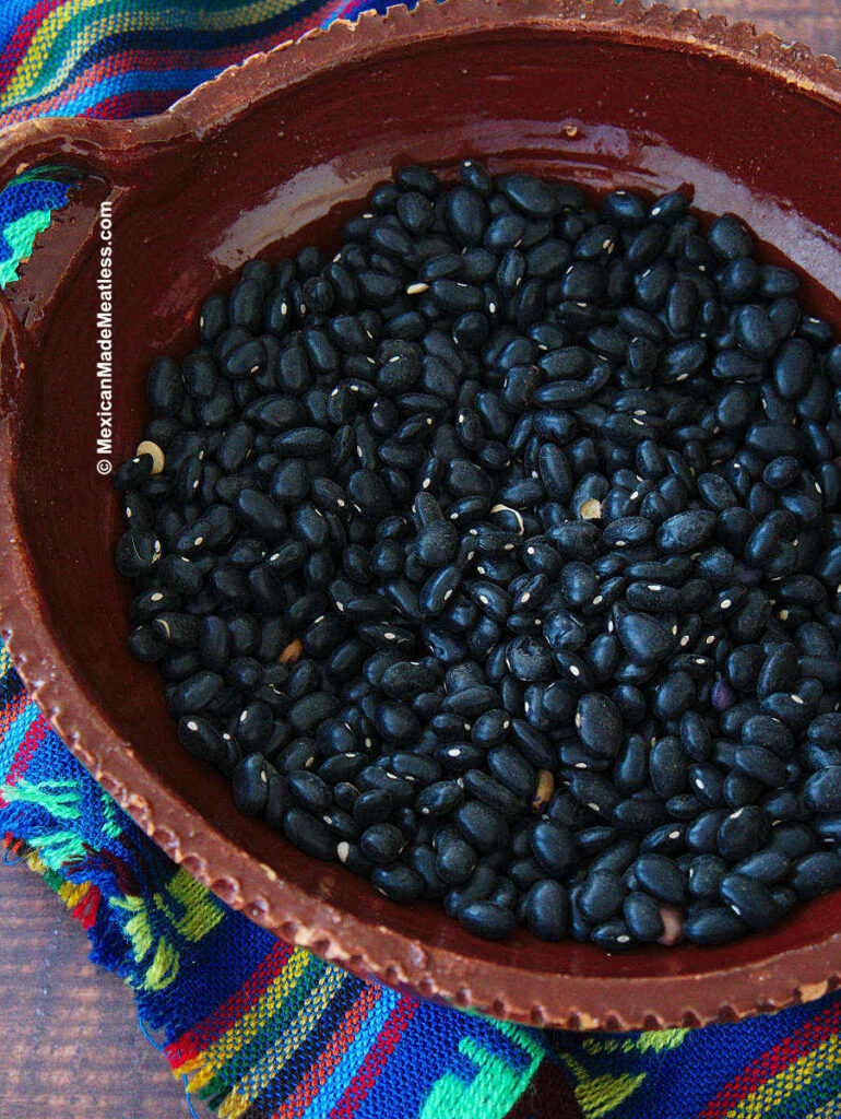 Dried Mexican black beans inside an earthenware bowl.