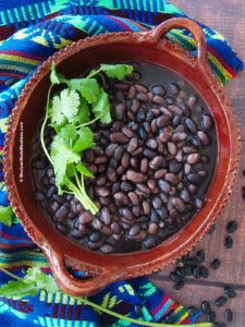 A brown bowl filled with cooked Mexican black beans and a sprig of fresh cilantro on top.
