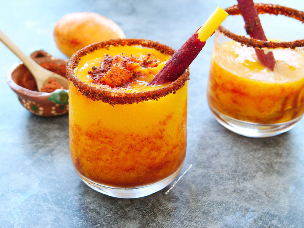 Mexican frozen mango sorbet drink called mangonada in a glass and drizzled with chamoy and Tajin.