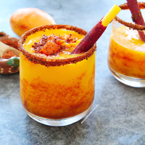 Mexican frozen mango sorbet drink called mangonada in a glass and drizzled with chamoy and Tajin.
