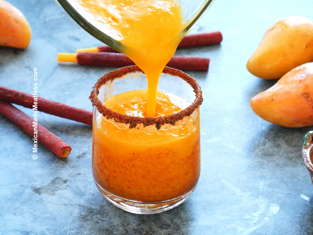 Pouring spicy mango slushy called mangonada into a small glass.