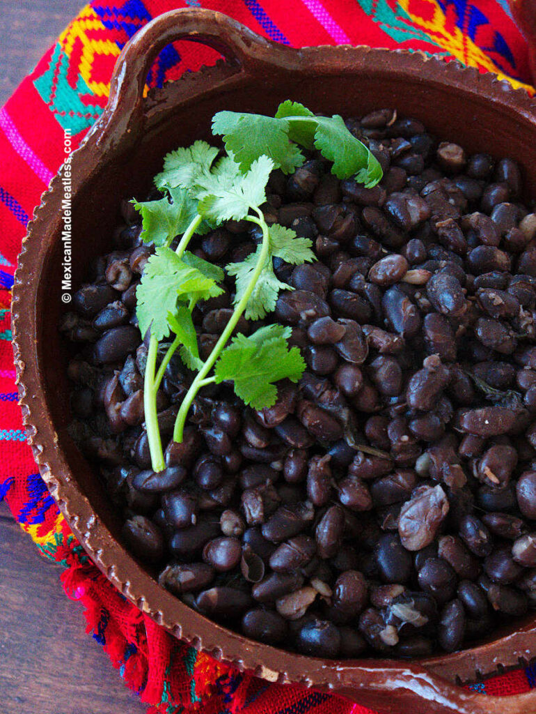 Cooked black beans inside brown bowl and decorative Mexican red cloth.