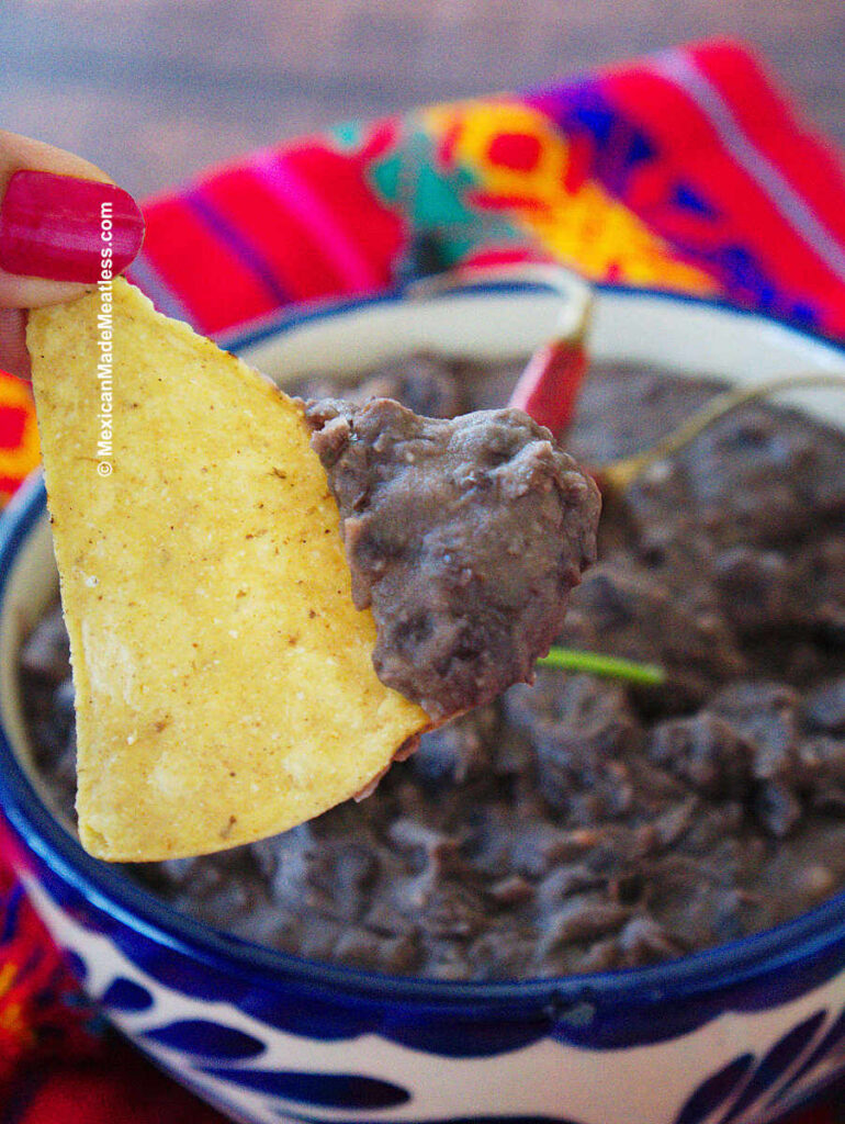 Dipping into refried black beans with a corn chip. 