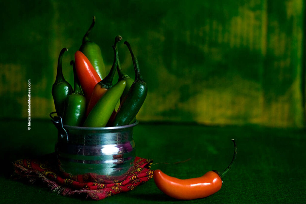 Green and orange chile peppers inside small metal bowl.