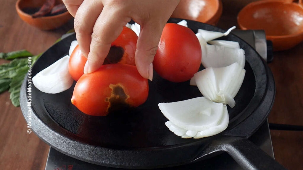 Roasting tomatoes and white onion pieces on a hot griddle to make salsa.