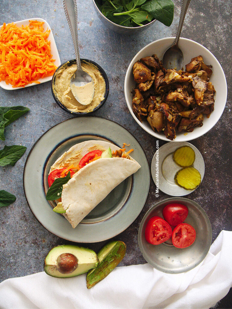 Mushroom shawarma wrap on a grey plate with hummus and topping on the side. 
