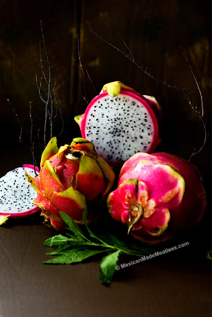 Fresh unpeeled dragon fruits and one sliced on a brown table.