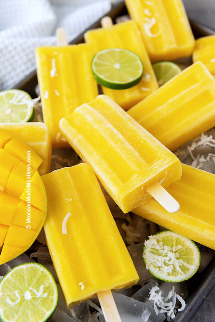 Coconut mango lime paletas stacked on top of ice cubes.