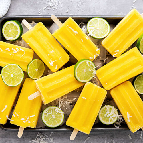 Mexican mango paletas laying on top of ice cubes on a metal tray.