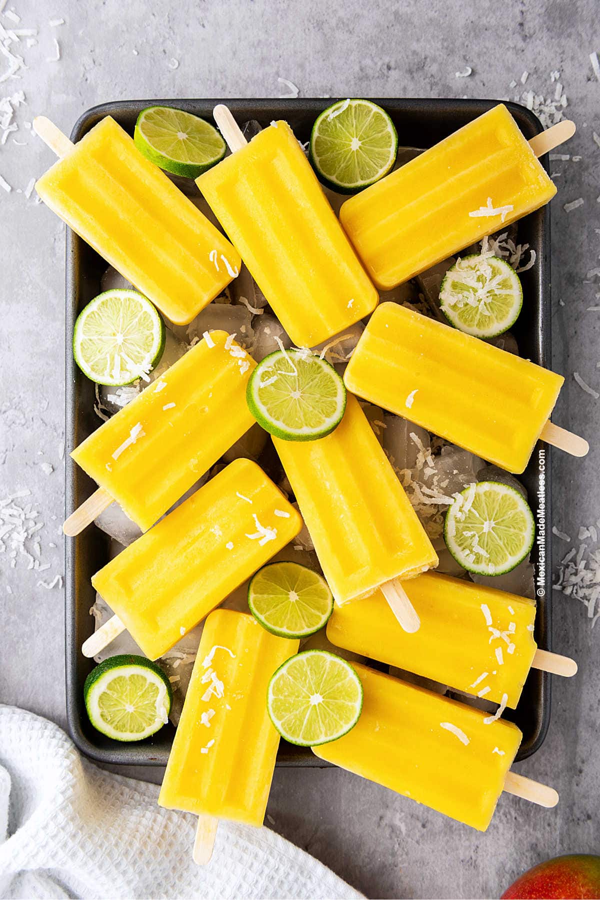 Creamy Mexican mango paletas or ice pops on a tray with lime slices.