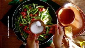 Seasoning green beans, onion, and tomatoes to make Mexican ejotes con huevo.