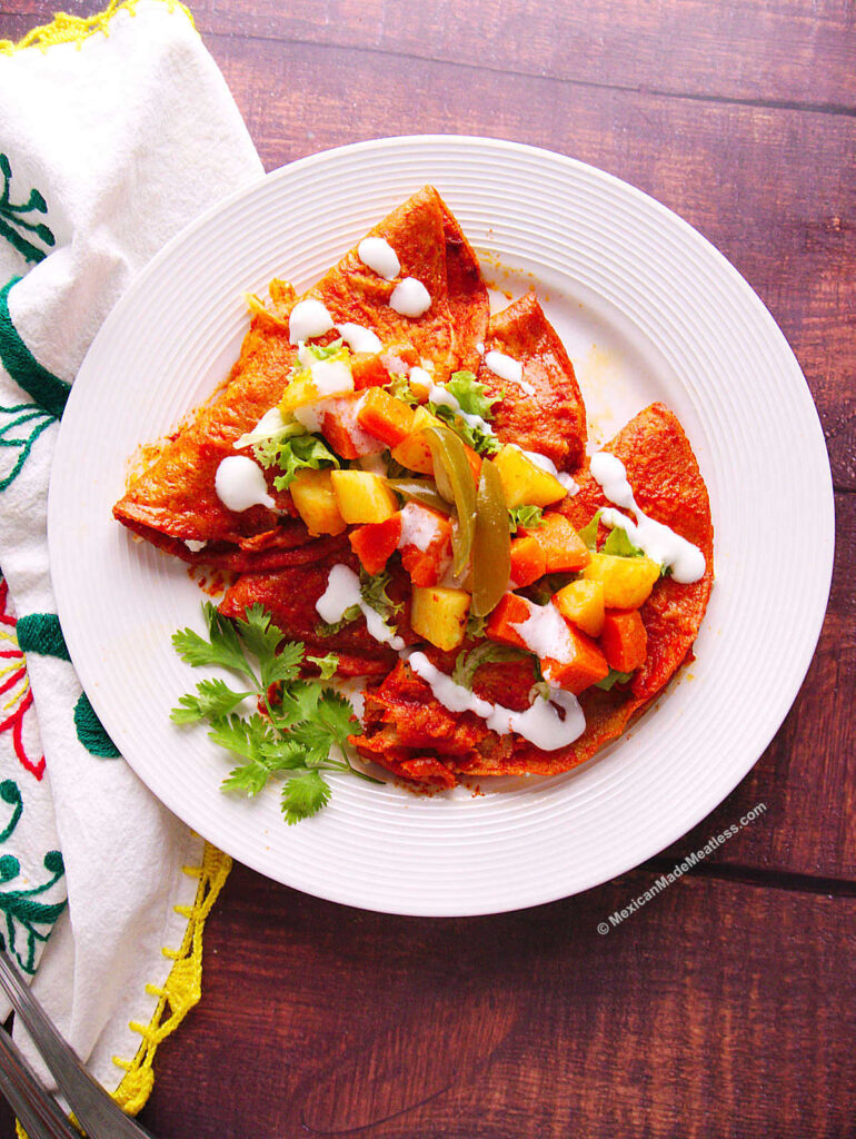 Three enchiladas Michoacanas or cheese filled enchiladas rojas topped with potato and carrot and Mexican crema.