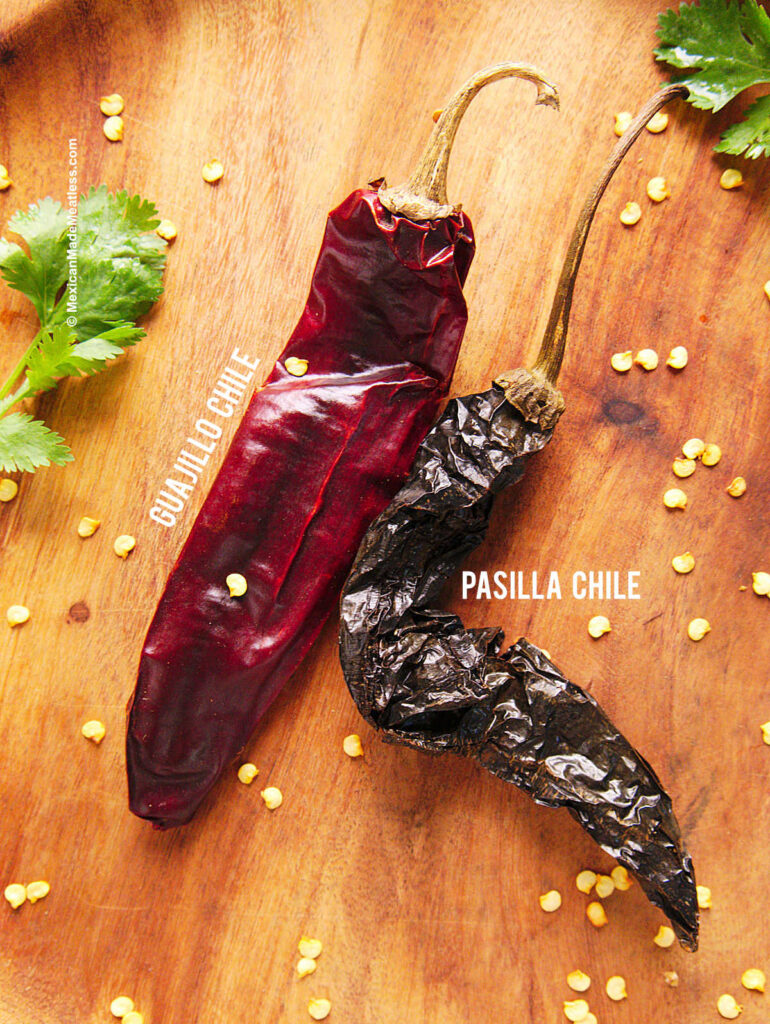 One pasilla pepper and one guajillo chile on a brown plate.