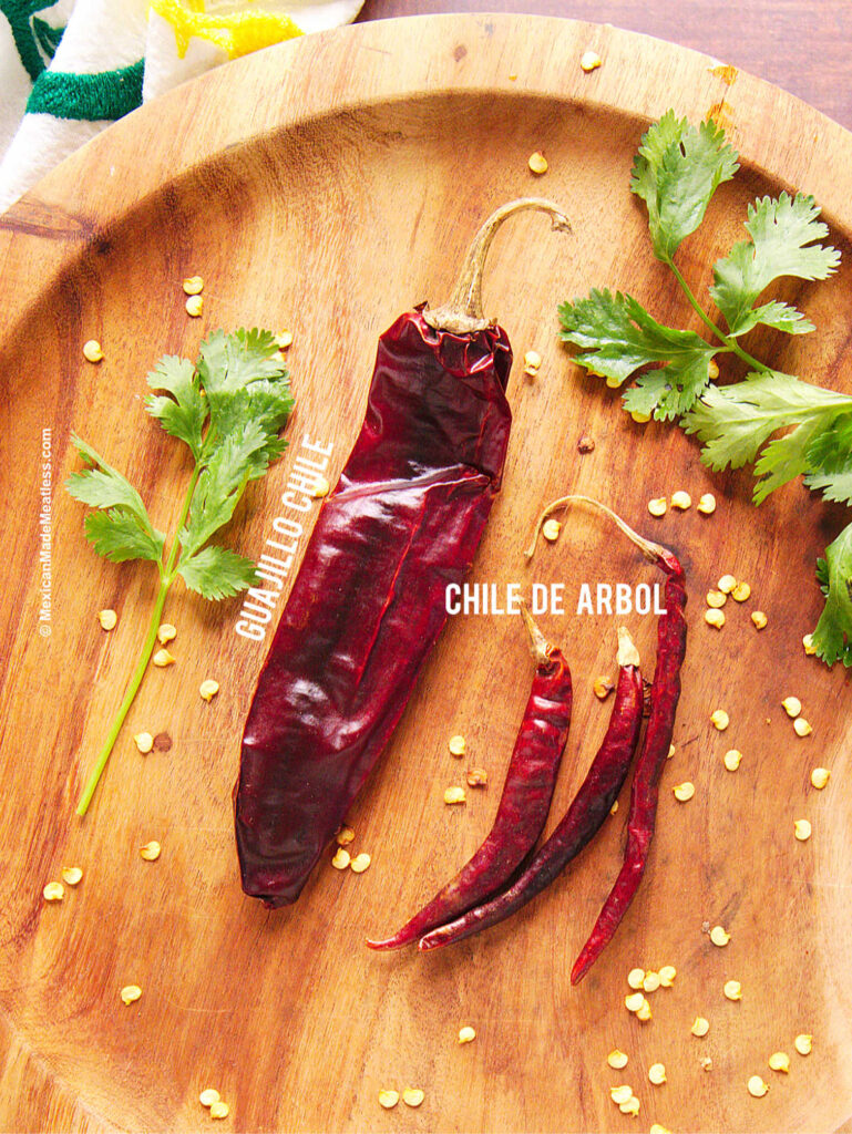 One chile guajillo and one chile de arbol on a wood plate.