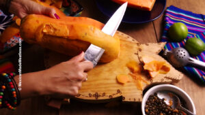 Peeling a papaya with a knife on a wood cutting board.