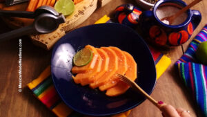 Fresh papaya slices sprinkled with salt and drizzled with lime juice inside a blue bowl.