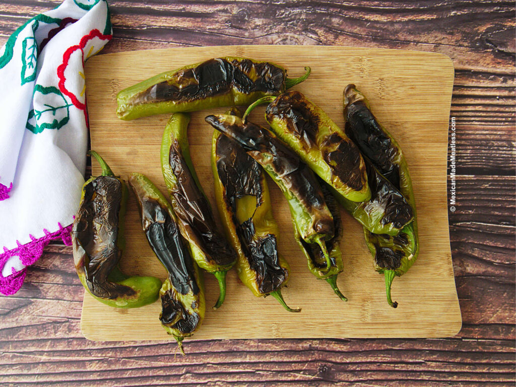 Roasted green hatch chiles on a wooden cutting board.