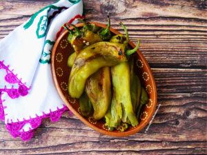 Roasted and peeled green hatch chiles inside a terracotta bowl.