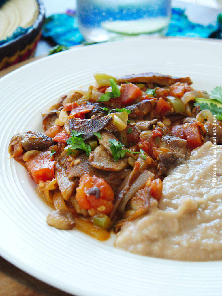 Vegan bistec a la mexicana served with refried beans on a white plate.